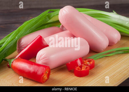 Cumulo di salsicce con cipolline e peperoncino su un tagliere con sfondo di legno Foto Stock