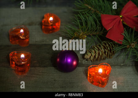 Composizione di natale di rami di abete decorato archi e le sfere con candele accese su uno sfondo di legno Foto Stock