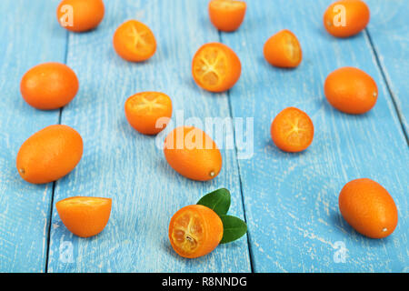 Cumquat o kumquat con metà sul blu sullo sfondo di legno Foto Stock