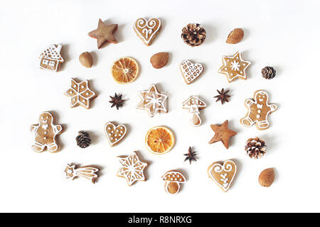 Natale decorativo modello alimentare. Composizione invernale di gingerbread cookies, anice stelle, pigne e arancio secco fette di frutta isolato sul tavolo bianco sullo sfondo. Appartamento laico, vista dall'alto. Foto Stock