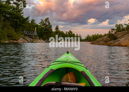 Il kayak sulle tranquille acque calme verso il sole di setting. Girato dal punto di vista del paddler.. Foto Stock