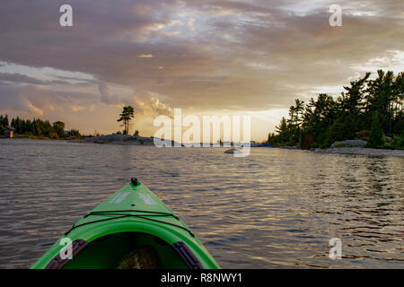 Il kayak sulle tranquille acque calme verso il sole di setting. Girato dal punto di vista del paddler.. Foto Stock