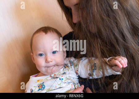 Una bambina tenuto da sua madre e giocando con la madre i capelli Foto Stock