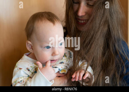 Una bambina tenuto da sua madre e giocando con sua madre capelli con sua madre sorridente al suo Foto Stock
