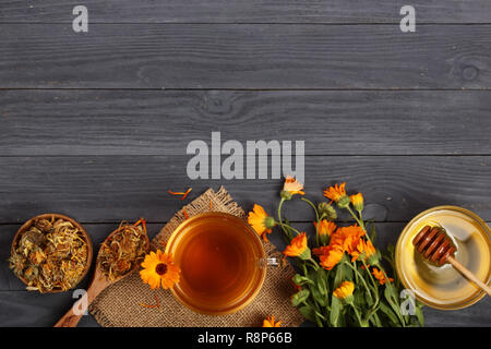 Calendula tè con fresca e fiori secchi su nero lo sfondo di legno con una copia dello spazio per il tuo testo. Vista superiore Foto Stock