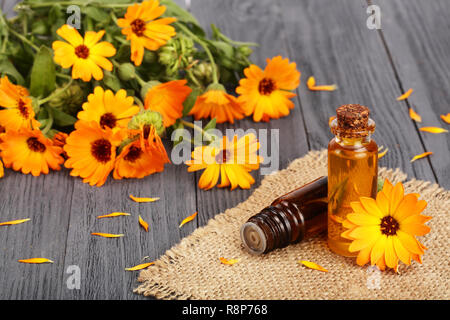 Aromaterapia olio essenziale con freschi fiori di tagete sul vecchio sfondo di legno. Olio di Calendula Foto Stock
