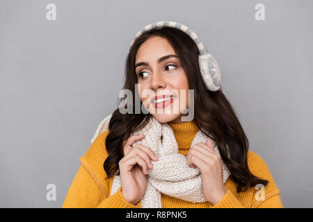Ritratto di donna bella indossare cuffie antirumore e sciarpa sorridente e toccando sciarpa isolate su uno sfondo grigio Foto Stock