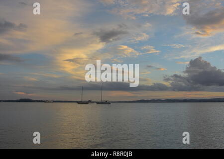 Superficie calma del porto di Waitemata riflettendo la luce solare con ormeggiate barche a vela e lontana terra in background in sera Nuvoloso. Foto Stock