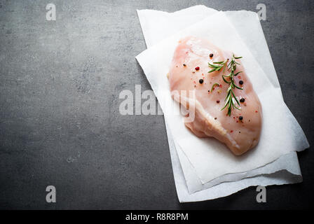 Filetto di pollo con spezie e rosmarino su un grigio scuro superficie. Vista dall'alto. Foto Stock