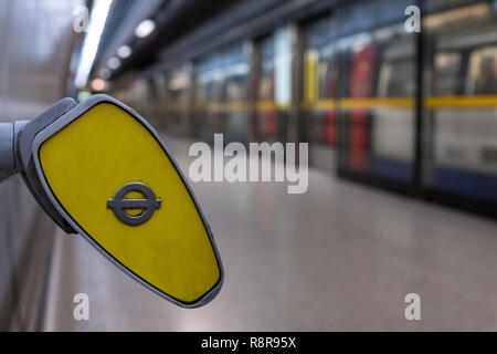 In primo piano, fine del mancorrente a Southwark stazione della metropolitana di Londra che mostra TFL roundel. Sullo sfondo sfocato treno arriva sulla piattaforma. Foto Stock