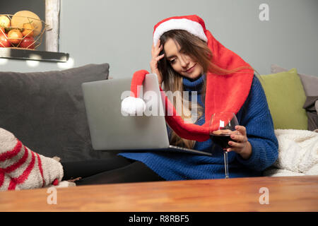 Ragazza solitaria in un cappello di Natale si beve vino seduti sul divano Foto Stock