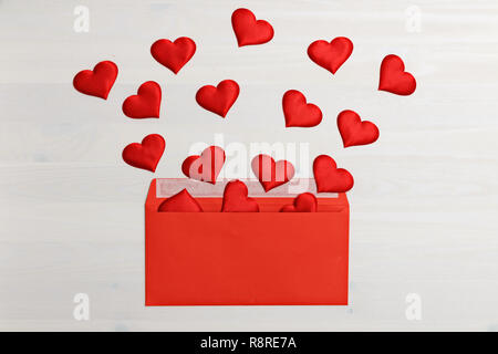 Primo piano della red cuori battenti fuori di una carta rossa busta su un bianco sullo sfondo di legno. Il giorno di San Valentino festa concetto Foto Stock