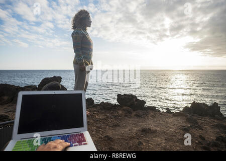 La tecnologia del computer portatile a internet con la scrittura a mano e di lavoro e di bella donna libera in piedi in background con la sensazione che il tramonto e godendo i n Foto Stock