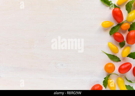 Cucina il concetto di sfondo con spazio di copia e la fila di rosso e giallo pomodori disposti in configurazione con cicoria verde foglie bianco su una superficie di legno. V Foto Stock