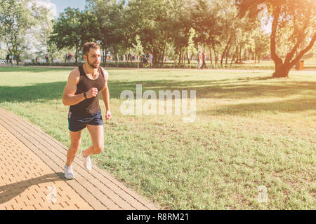 Atletica Giovane uomo in esecuzione in natura. Uno stile di vita sano. Barbuto dai capelli nero sportivo è in esecuzione su strada - tramonto back lit Foto Stock