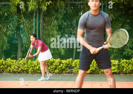 Giovane donna asiatica di giocatore di tennis pronto a servire in un misto di partita doppia Foto Stock