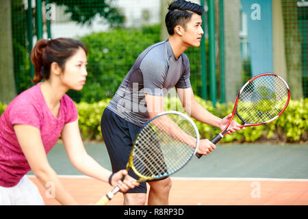 Giovane coppia asiatica di un uomo e di una donna i giocatori di tennis in un doppio misto corrispondono, concentrarsi sullo sfondo l'uomo Foto Stock
