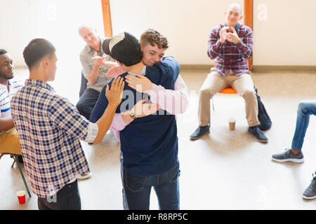 Gli uomini abbraccia e battendo le mani in una terapia di gruppo Foto Stock