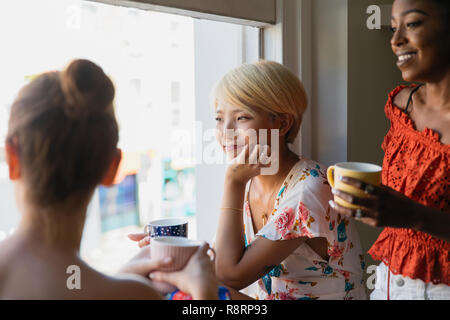 Giovani donne gli amici a bere un caffè a finestra appartamento Foto Stock