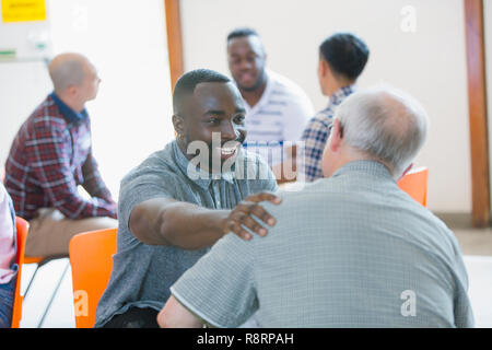 Sorridente, uomo felice di parlare, confortando l uomo nella terapia di gruppo Foto Stock