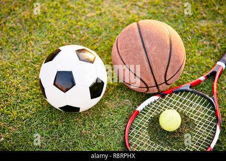 Il calcio pallone da calcio Basket Tennis palla e racket prevista sull'erba al tramonto, primo piano Foto Stock