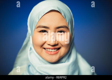 Close up ritratto sorridente, fiducioso giovane donna indossa seta blu hijab Foto Stock