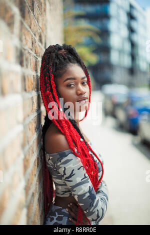 Fiducioso Ritratto di giovane donna con lunghe trecce di colore rosso sul marciapiede urbano Foto Stock