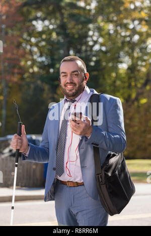 Imprenditore con minorazione visiva ascoltando il suo telefono e utilizzando la canna da zucchero Foto Stock