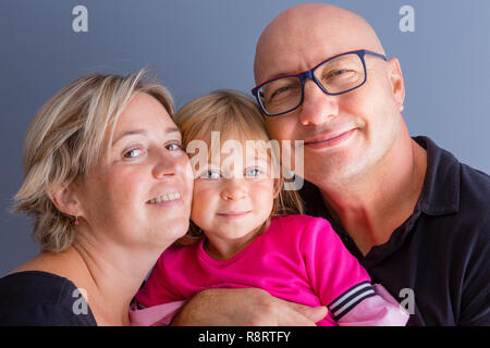 Close-up busto ritratto di famiglia con i genitori e la giovane figlia. Bold uomo in bicchieri, la sua bionda moglie e figlia in abito rosa appeso vicino e smilin Foto Stock