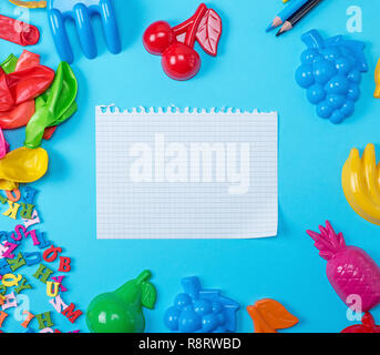 Foglio bianco strappato al di fuori del blocco note su uno sfondo blu nel mezzo di giocattoli infantile, spazio di copia Foto Stock