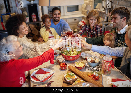 La famiglia felice e amici il tintinnio dei bicchieri cena di Natale e gustare in vacanze Foto Stock