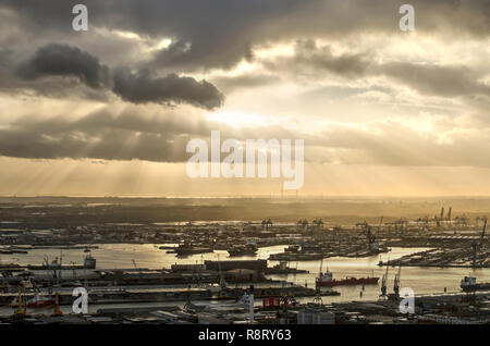 Rotterdam, Paesi Bassi, 10 Dicembre 2018: Drammatico cielo sopra Waalhaven harbour con i raggi del sole che splende attraverso l'apertura nel buio pioggia nuvole Foto Stock