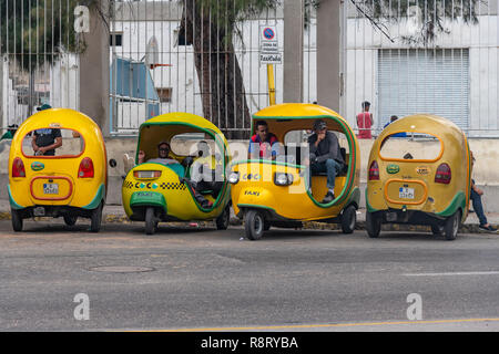 Cuban coco taxi driver avente una pausa prima di iniziare la ricerca per più passeggeri nella loro distintivo giallo taxi. L'Avana Cuba Foto Stock