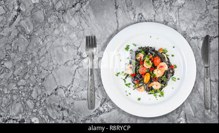 Nero Seppia Fettuccine con gamberi o gamberetti pomodori ciliegia, prezzemolo, peperoncino in vino e salsa di burro. Vista dall'alto in granito con copia spazio. Foto Stock