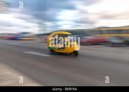 Donna cubana alla guida di una accelerazione di colore giallo brillante coco taxi in Havana Cuba Foto Stock