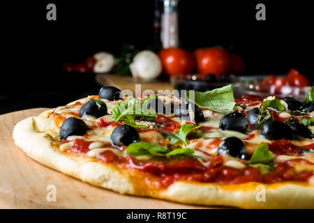 Pizza cotta al forno con salame salsiccia per pizza, olive nere, basilico e mozzarella. Foto Stock