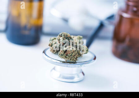 Primo piano di alcune gemme marihuana sul diaframma di uno stetoscopio collocato sul tavolo di un ufficio medici Foto Stock