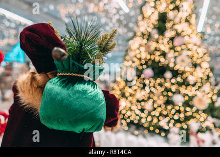 Santa da dietro con borsa regalo su sfondo bokeh di albero di natale. Foto Stock