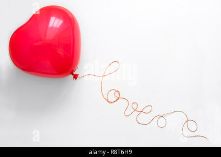 Concetto creativo. Mano azienda cuore rosso forma palloncino con amore la parola dal filo bianco su sfondo di legno. Lay piatto. Vista dall'alto. Il giorno di San Valentino celeb Foto Stock