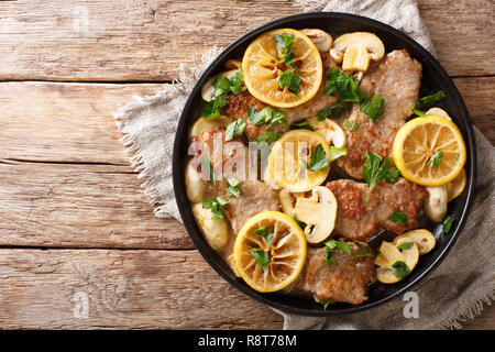 Cucina Italiana il filetto di vitello scaloppini con funghi e limoni in salsa di close-up in una padella sul tavolo. Parte superiore orizzontale vista da sopra Foto Stock