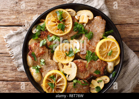 Italiano corso principale scaloppini di vitello cucinato con i funghi e i limoni in una salsa piccante, close-up in una padella sul tavolo. Parte superiore orizzontale vista da sopra Foto Stock