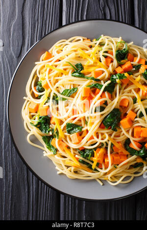 Organici pasto spaghetti con la zucca, gli spinaci e il formaggio cheddar close-up su una piastra sul tavolo. Verticale in alto vista da sopra Foto Stock