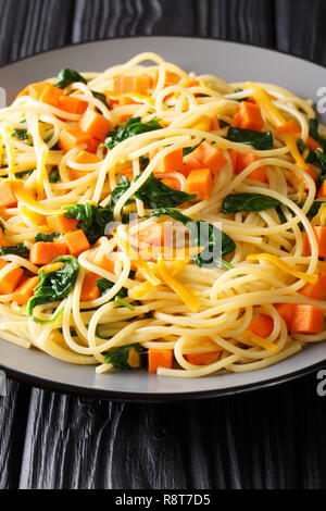 Vegetariana Italiana spaghetti con la zucca, gli spinaci e il formaggio cheddar close-up su una piastra sul piano verticale. Foto Stock