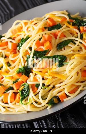 Spaghetti con la zucca, gli spinaci e il formaggio cheddar close-up su una piastra sul piano verticale. Foto Stock