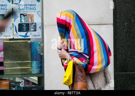 Preston, Lancashire, Regno Unito Meteo. Dic 2018. Wet & ventoso giorno per i clienti di Natale costringendo la donna a prendere la copertura sotto una coperta multicolore a strisce dalla pioggia pesante. Credit; MediaWorldImages/AlamyLiveNews Foto Stock