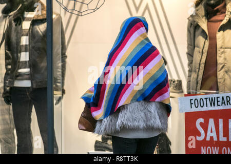 Preston, Lancashire, Regno Unito Meteo. Dic 2018. Wet & ventoso giorno per i clienti di Natale costringendo la donna a prendere la copertura sotto una coperta multicolore a strisce dalla pioggia pesante. Credit; MediaWorldImages/AlamyLiveNews Foto Stock