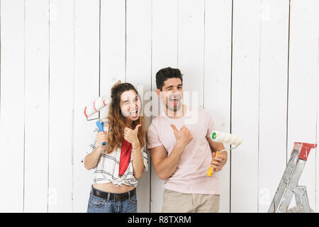 Foto di bella giovane uomo e donna pittura muro bianco e facendo lavori di rinnovo utilizzando rulli di vernice Foto Stock