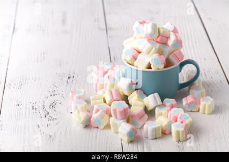 Marshmallows colorati in una tazza, su uno sfondo di legno Foto Stock