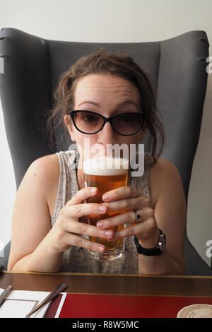 Donna con occhiali da sole sorseggiando una birra in un caffè Foto Stock
