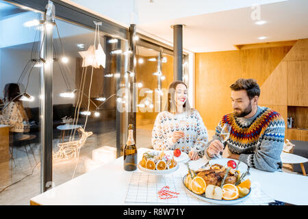 Coppia giovane avente una cena di gala seduti insieme nella casa moderna durante le vacanze invernali Foto Stock